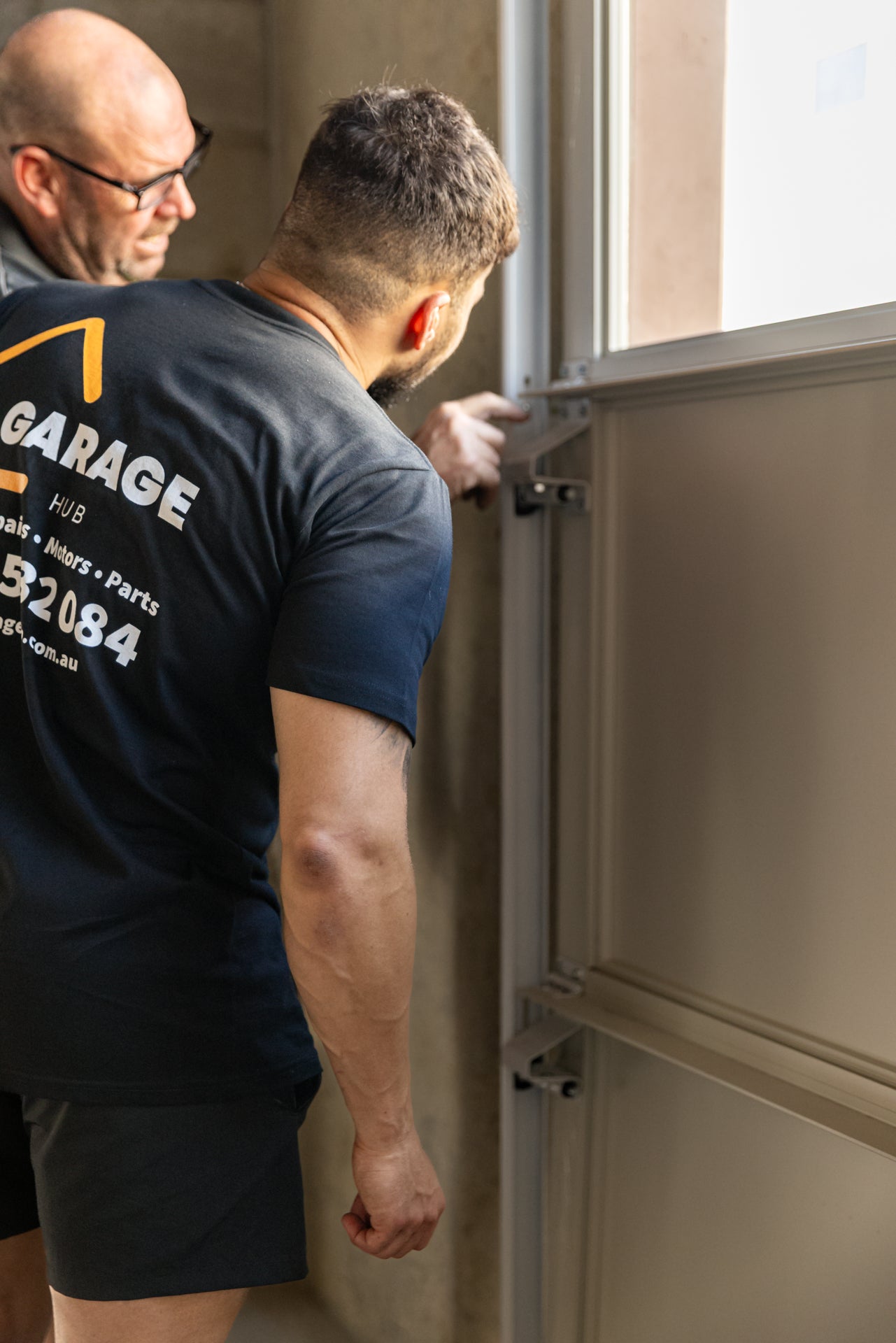 Garage technicians inspecting garage door with faulty hinge