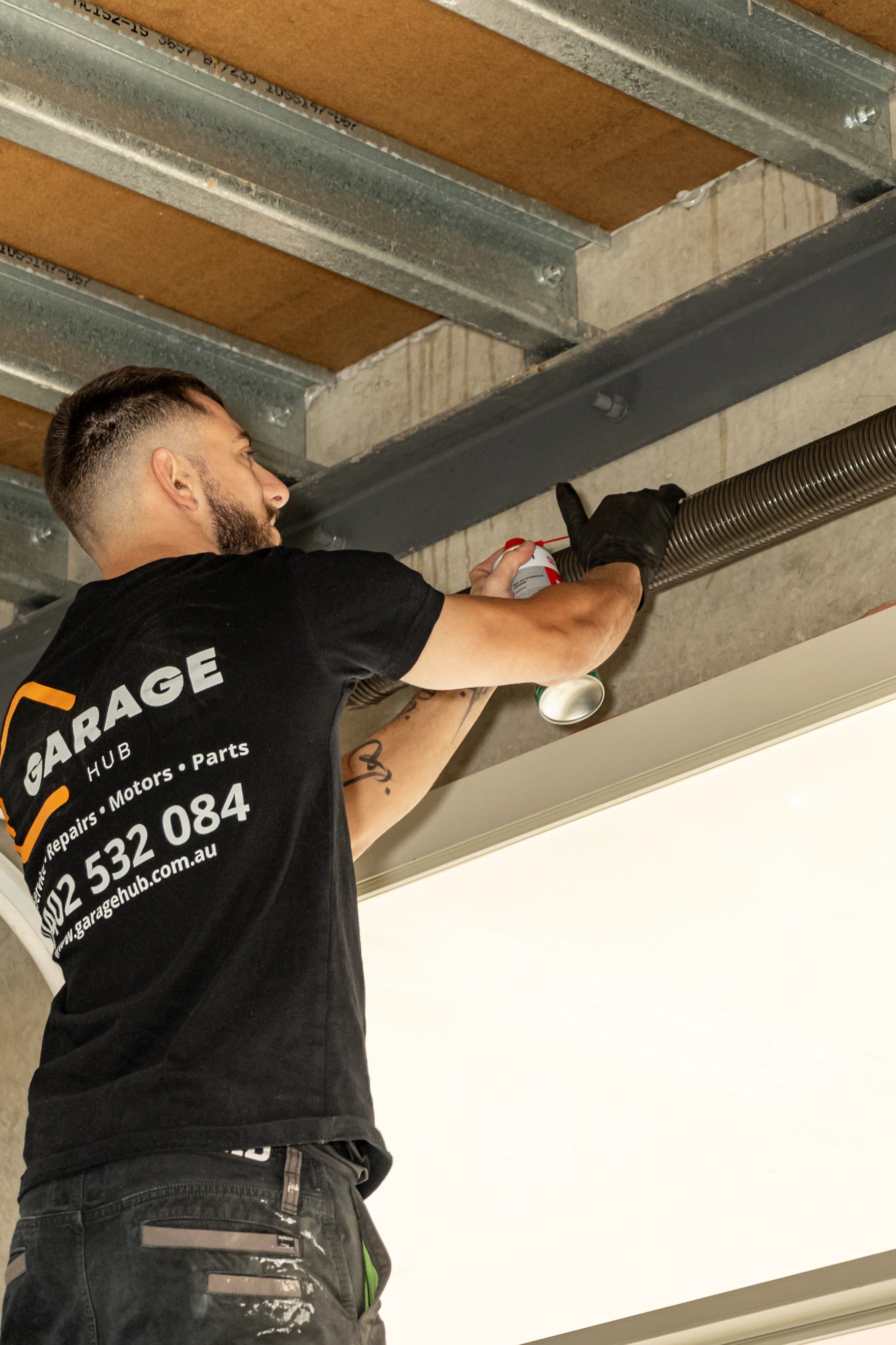 Garage technician working on a garage door with 'Garage Hub' t-shirt.