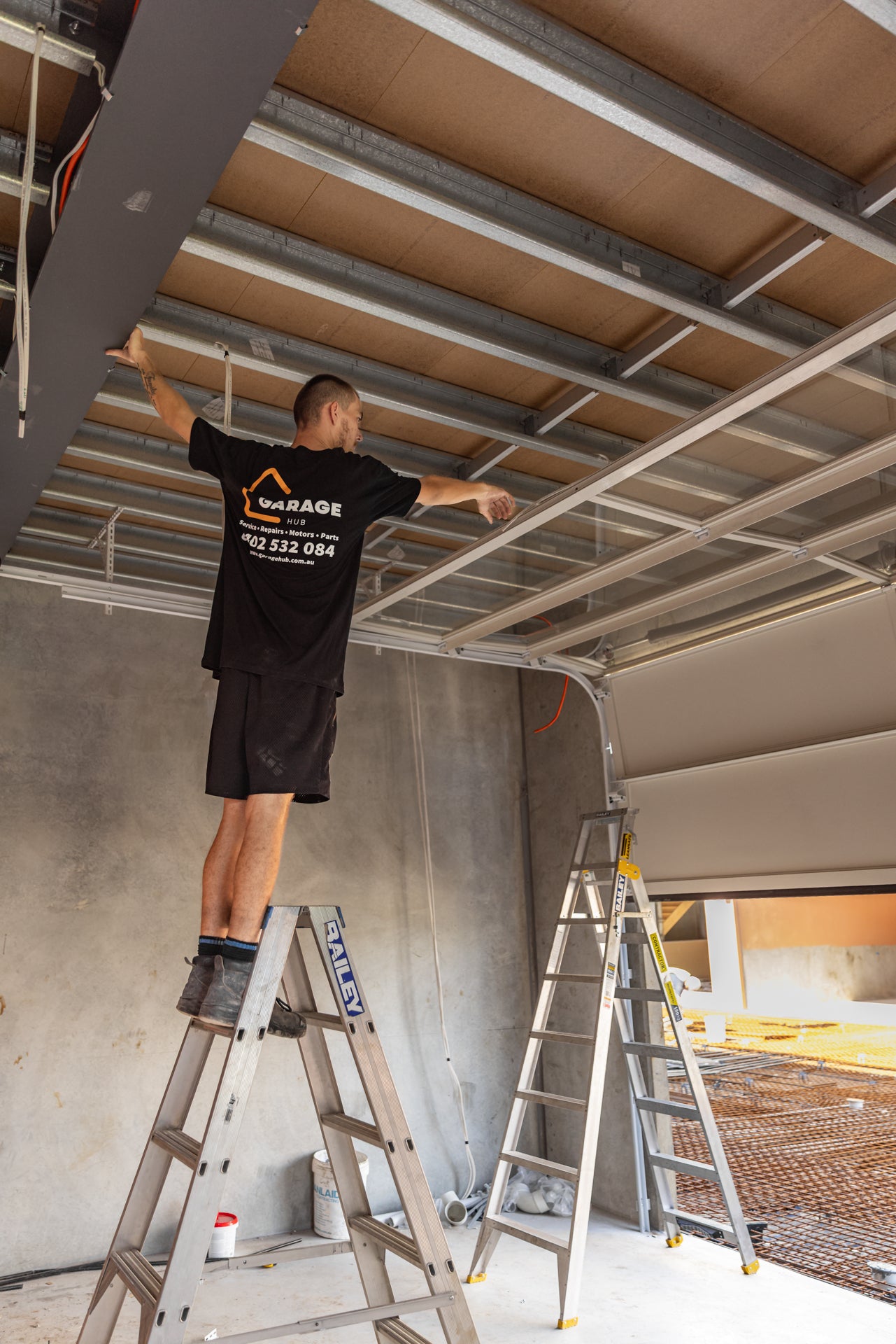 Garage hub technician inspecting garage door panels on a ladder.