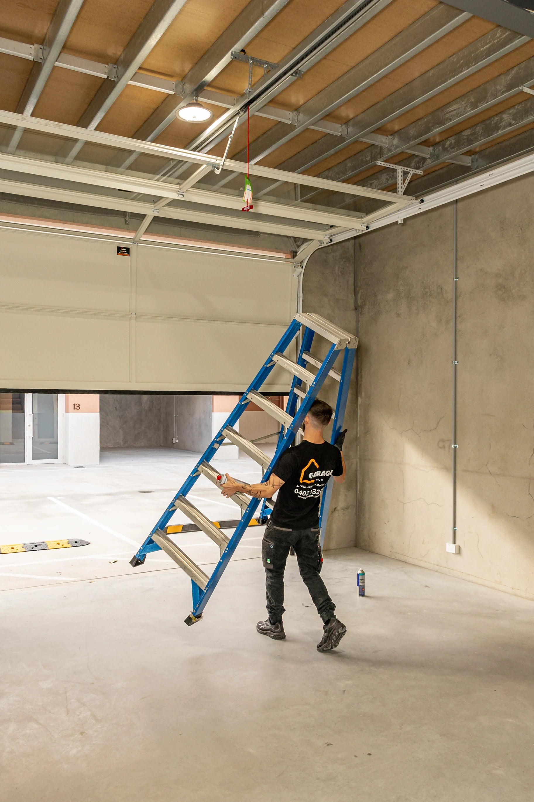 Garage technician with a ladder in an unfinished room with exposed ceiling beams, ready to service a garage door.